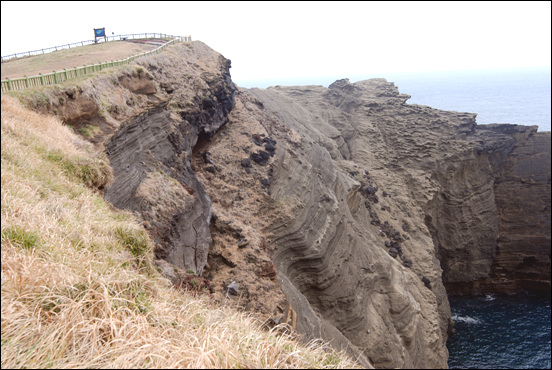 남쪽 절벽에 노출된 사층리와 현무암. 사층리는 응회환의 외륜이 침식되어 노출된 것이고, 현무암은 용암연을 이루던 암석이 깎여 노출된 것이다.