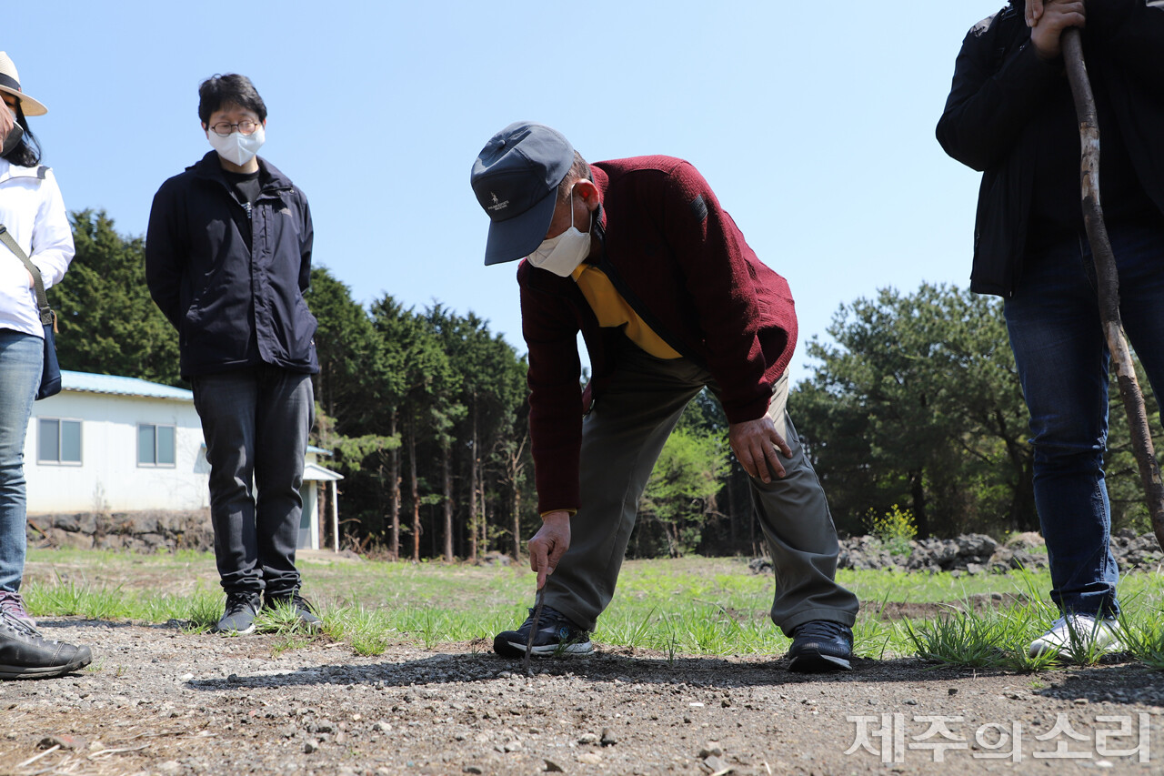 땅에 나뭇가지로 그려가며 목장 위치와 인근 지형을 설명하고 있는 권기홍 전 노인회장. ⓒ제주의소리