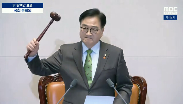 윤석열 대통령 탄핵소추안 표결 결과를 발표, 가결을 선포하며 의사봉을 두드리고 있는 우원식 국회의장. 그는 역사적 순간, 왼쪽 가슴에 국회의원 배지와 제주4.3을 상징하는 동백꽃 배지를 달았다. 사진=MBC 뉴스 공식 유튜브 갈무리. 